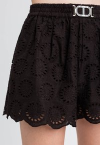 Pantaloni corti neri ricamati con orlo a scallop, caratterizzati da motivi floreali e una vita elastica arricciata con un dettaglio di fibbia in argento.