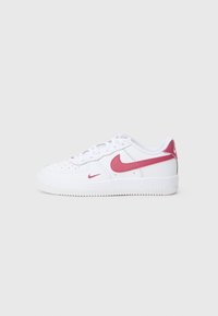 Biezi balti Nike apavi ar rozā Swoosh logotipiem un baltiem šņorēm uz vienkārša gaiši pelēka fona.