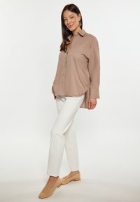 Beige kauluspaita, jossa napit edessä, yhdistetty valkoisiin istuviin housuihin ja vaaleanruskeisiin loafer-kengiin. Silkkinen pinta rentouttavalla istuvuudella.