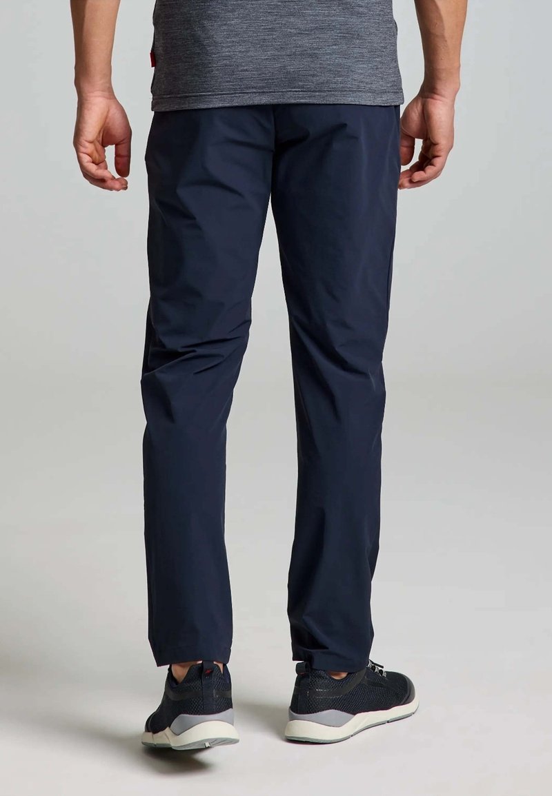 Pantalons bleu marine à coupe fuselée, fabriqués en tissu léger. Comprend une taille élastique et des zips aux chevilles. Associés à des baskets noires.
