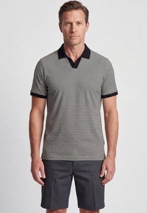 Man wearing a gray short-sleeve polo shirt with black collar and sleeve trim, paired with dark gray shorts, standing against a plain background.