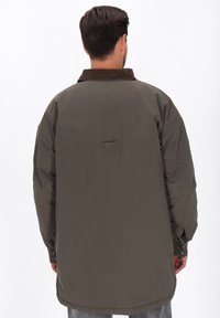 Oliven grøn, oversized jakke med kordfløjlskrave, der har en hængekrog bagpå og knapmanchetter. Glat, tekstureret stof.