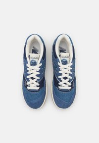 Blå denim sneakers med vita snören, med blandade texturer av släta och grova tyger, vadderad krage och en logotyp på tungan.