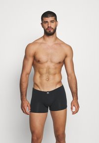 Zwarte boxershorts van zacht materiaal, met een middelhoge tailleband en een strakke pasvorm, die een gladde, matte textuur benadrukken.