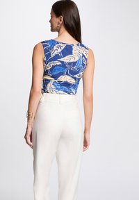 Haut sans manches en bleu avec un imprimé de feuilles beige ; associé à un pantalon blanc taille haute. Texture lisse avec un design ajusté.