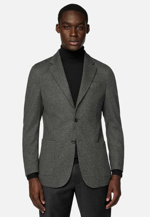 Grau karierter Blazer mit zwei Knöpfen, Reverskragen und aufgesetzten Taschen, kombiniert mit einem schwarzen Rollkragenpullover und dunklen Hosen.