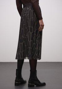 Plissé rok in donkergrijs met zwart geometrisch patroon. Elastische tailleband met merkdetails. Gecombineerd met zwarte enkellaarzen.