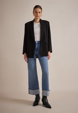 Black blazer with two buttons, white fitted shirt, and high-waisted blue jeans with rolled cuffs. Black pointed-toe heeled boots with studs.