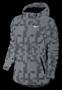 Veste Nike en noir et blanc avec un motif de points réfléchissants, dotée d'une capuche, de poches zippées et de poignets élastiqués pour un ajustement confortable.