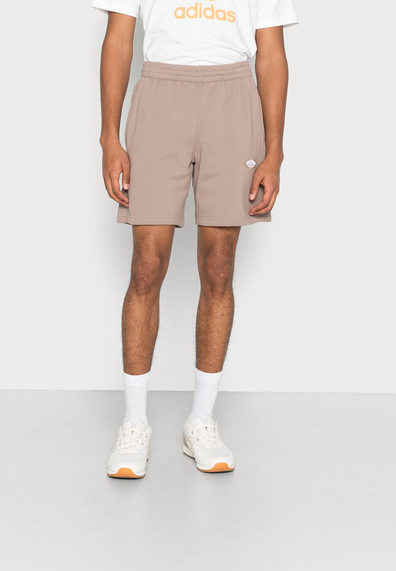 Beiga herrshorts med elastisk midja, sidofickor och en liten logotyp-patch. Matchas med vita strumpor och ljusa sneakers.