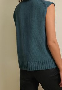 Sleeveless sweater in deep teal, made of soft knit material. Features a ribbed hem and a relaxed fit. Simple design with minimal stitching.