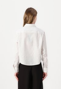 Camicia a righe in cotone con colletto, maniche lunghe e orlo posteriore corto. Presenta sottili linee verticali di colore bianco e tonalità chiare.