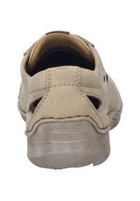 Vaalean beige nahkainen kenkä, jossa on leikkauksia ja teksturoitu kumipohja. Ominaisuuksiin kuuluu pyöristetty takaosa ja näkyvät ompeleet.