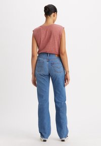 Rode heidelook mouwloos shirt gecombineerd met hoge taille blauwe jeans met een rechte pijp, achterzakken en een logo patch op de tailleband.