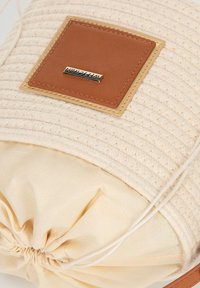 Ronde, geweven tas in lichtbeige met een tan leren accentlabel; trekkoordsluiting met een gladde, crèmekleurige binnenvoering.