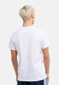 Vit bomulls t-shirt med korta ärmar, rundad halsringning och en rektangulär etikett på övre delen av ryggen. Tyget verkar mjukt och slätt.