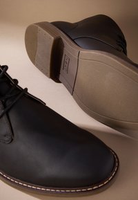 Čierne kožené topánky s okrúhlou špičkou, koženými šnúrkami, kontrastným prešívaním a textúrovanou gumovou podrážkou. Minimalistický dizajn bez ďalších vzorov.