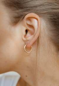 Pendiente de aro dorado con una textura suave y brillante, que presenta un diseño circular simple. Se lleva en el lóbulo, acentuando la oreja.