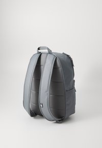 Mochila cinza com alças acolchoadas, uma textura suave e compartimentos com fecho éclair. Apresenta uma pega na parte superior e bolsos laterais para armazenamento.