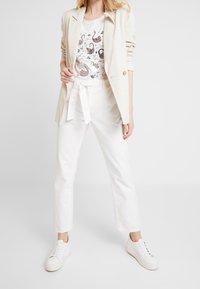 Blazer de lino beige, camiseta gráfica blanca con estampado de animales, pantalones blancos de talle alto con cinturón de lazo y zapatillas blancas.