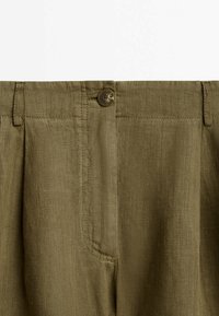 Olive green linen trousers featuring a front button closure, pronounced pleats, and set-in side pockets. Textured fabric with a smooth finish.