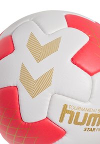 Pallone da calcio bianco e rosso con motivo a stelle, accenti a zig zag dorati, superficie liscia e branding stampato. Cuciture e pannelli visibili.