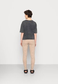 Camisa cinza escura de mangas curtas combinada com leggings bege com um padrão preto espalhado, finalizada com sandálias pretas.