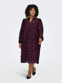 Spetsklänning i mörklila med långa puffärmar, v-ringning och blommiga utskurna mönster längs fållen. Bärs med svarta ballerinas.