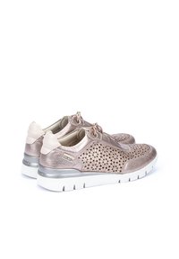 Zapatos deportivos metálicos en color oro rosa con diseño perforado, acentos en crema, cordones elásticos y suelas de goma blanca. Cuentan con una plantilla acolchada.