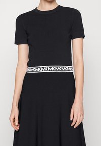 Abito nero con maniche corte, top aderente e gonna svasata. Presenta una banda con logo bianco attorno alla vita. Tessuto liscio, design casual.