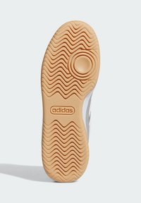 Súprava tenisiek Adidas so svetlohnedou gumovou podrážkou s vlnitým dezénom, zaoblenými akcentmi a brandingom. Čistý, minimalistický dizajn s textúrovaným povrchom.