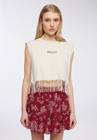 Top in crema a maniche corte con orlo in frange e grafica "BREATHE"; abbinato a una gonna a balze rossa con motivo floreale.