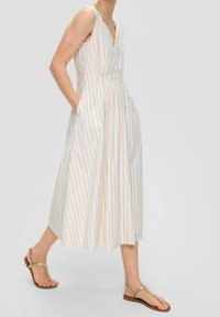 Vestido sin mangas, a rayas en blanco y dorado, con escote en V y cintura fruncida. Presenta bolsillos laterales y una falda fluida hasta la rodilla.