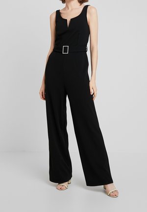 Sort jumpsuit med v-udskæring, ærmeløs design, brede ben og et stofbælte med en kvadratisk smykke spænde. Glat tekstur.