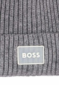 Berretto grigio lavorato a maglia con texture a coste verticali e una toppa rettangolare con il testo bianco "BOSS". Materiale in morbida lana.