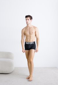 Boxers noirs ajustés avec une large ceinture de marque "DIESEL" blanche, au design ajusté, texture lisse et style minimaliste sur fond neutre.