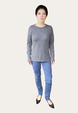Un pull en tricot gris à manches longues, associé à un pantalon slim-fit bleu clair et des chaussures noires à bout pointu, sur un fond clair.