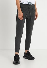 Gray, tapered sweatpants with an elastic waistband and drawstring. Smooth texture with side pockets. Paired with black athletic sneakers.