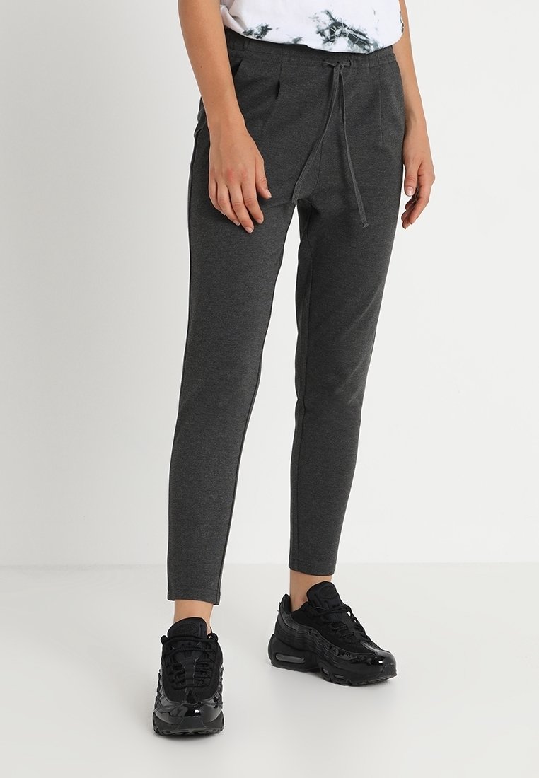 Gray, tapered sweatpants with an elastic waistband and drawstring. Smooth texture with side pockets. Paired with black athletic sneakers.
