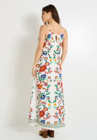 Vestido maxi con un patrón floral en rojo, amarillo y azul sobre un fondo blanco. Presenta tirantes ajustables y un pequeño ojal en la parte posterior.