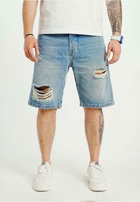 Jeansshorts i ljusblått med slitna detaljer. Har revor vid knäna och en rak skärning. Matchas med vita sneakers.