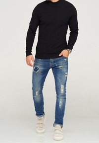 Pull en maille noire, jean bleu déchiré et baskets beiges à scratchs. Tenue décontractée avec des textures contrastées.