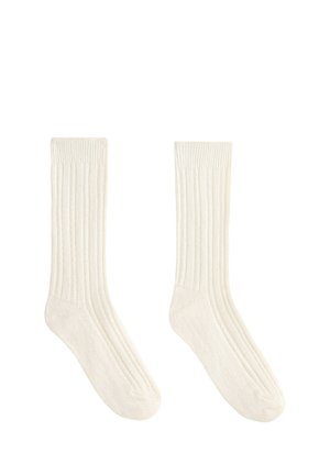 Paire de chaussettes blanches unies côtelées, à mi-mollet, posées à plat avec la bordure, le talon et l'orteil visibles sur fond blanc.