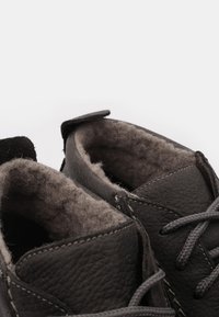 Scarpe in pelle grigia con una morbida fodera pelosa. Caratterizzate da una forma arrotondata, cuciture in contrasto e lacci piatti. Accentuate da una linguetta in suede.