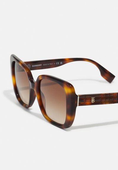Šelako spalvos saulės akiniai su storesniu rėmeliu, gradientiniais rudo atspalvio lęšiais ir tekstūruotomis rudo rašto kojelėmis, puoštomis auksiniu Burberry logotipu.