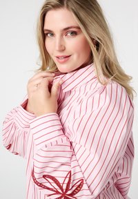 Roze gestreept shirt met rode en witte strepen, met een bloemenborduursel op de mouw en een klassieke knoopsluiting kraag.