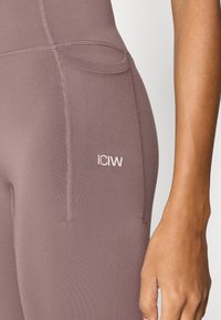 Ελαστικό, μωβ κολάν με ραμμένες ραφές και μικρό λευκό λογότυπο "ICIW". Διαθέτει πλαϊνή τσέπη για ευκολία. Μαλακή, λεία υφή.