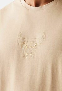 T-shirt in cotone beige con un logo di toro ricamato in rilievo di una tonalità più chiara. Collo rotondo e texture morbida e liscia.