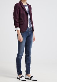 Burgundy kavaj med slag, i kombination med randig blå och vit topp, mörka denimjeans och svartvita sneakers.