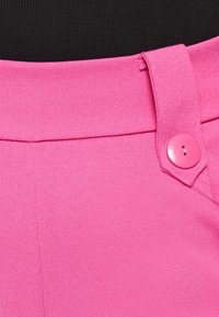 Höga ljusrosa byxor med en matchande knapp på bältesöglan, bärs med en svart topp.